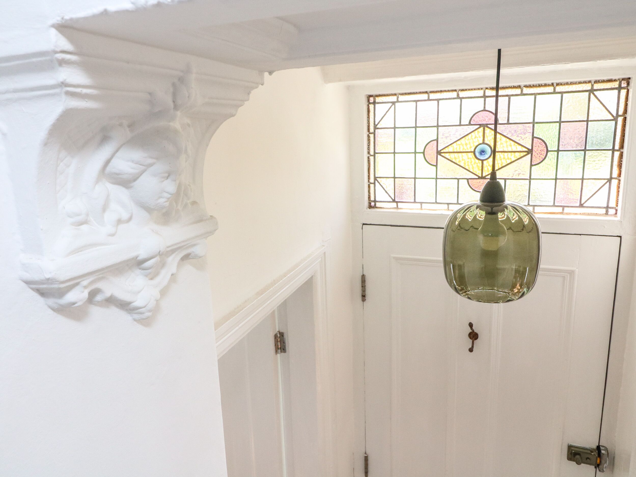 Une porte blanche ornée d’un vitrail et surmontée d’un luminaire suspendu.