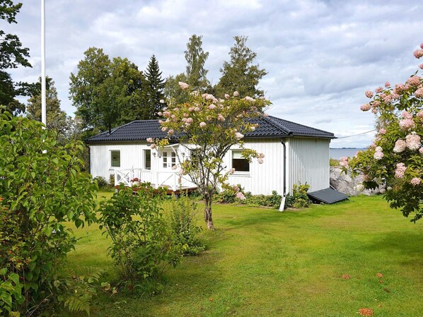 A white wooden house with a black roof, surrounded by a well-maintained lawn and flowering trees. - 4 Star Holiday Home in Odensbacken (Odensbacken)