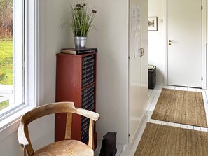 A room with a wooden chair, a metal bookcase, a potted plant, a door with a mat, and a window with a view of greenery. - 4 Star Holiday Home in Odensbacken (Odensbacken)