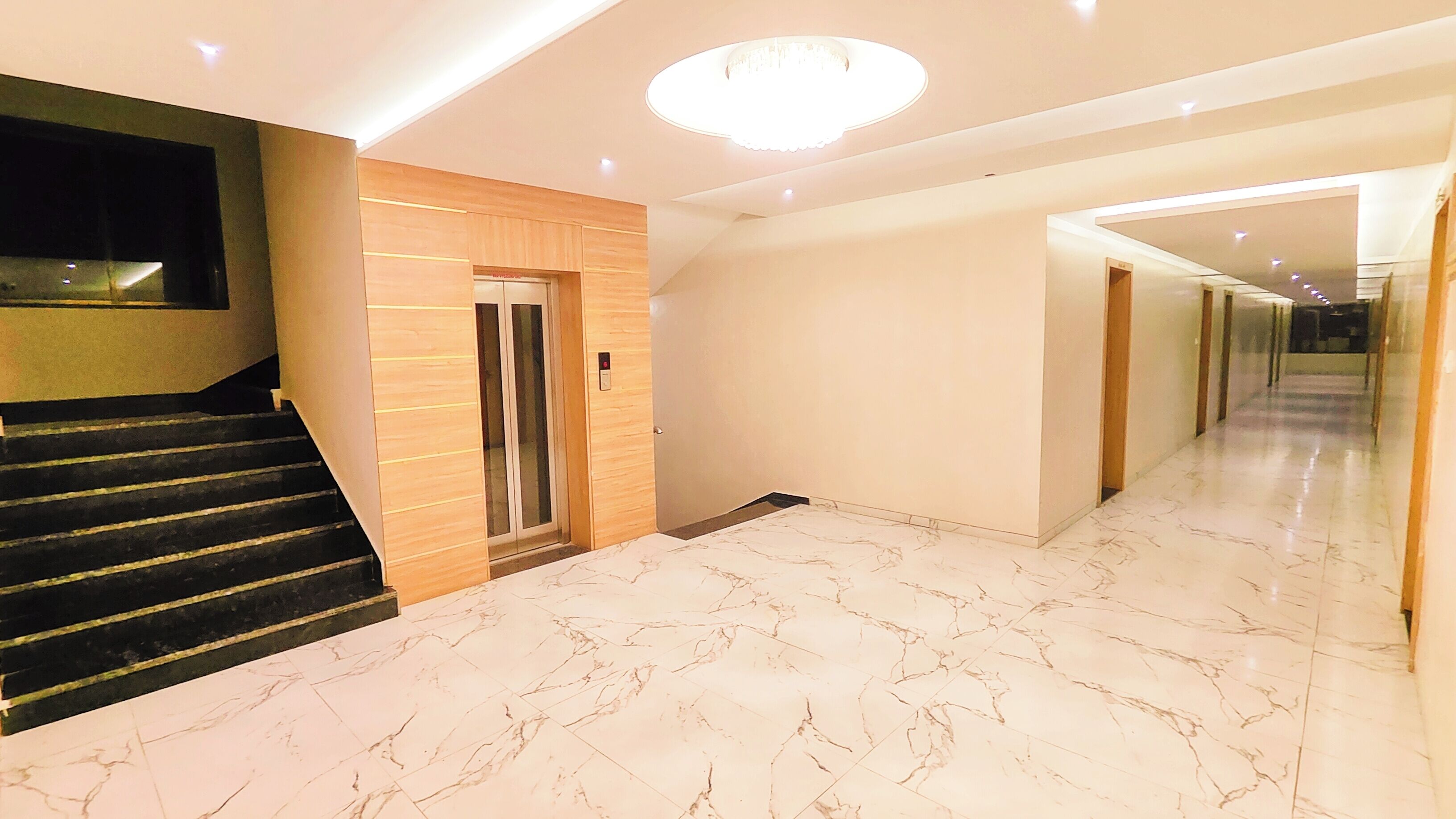 Um corredor moderno com piso de mármore, escada com degraus pretos e painel de parede em madeira.