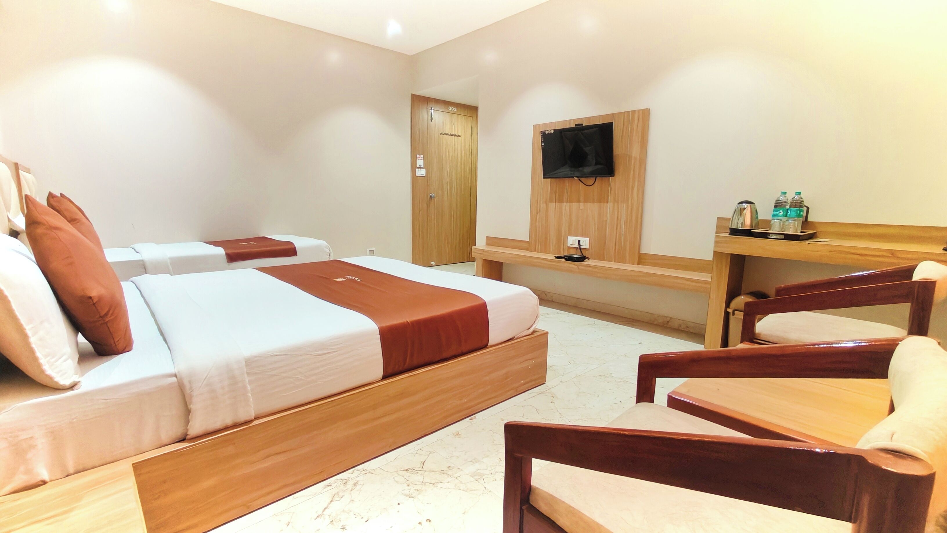 A hotel room with two beds, a wooden desk, a chair, a TV, and a minibar.