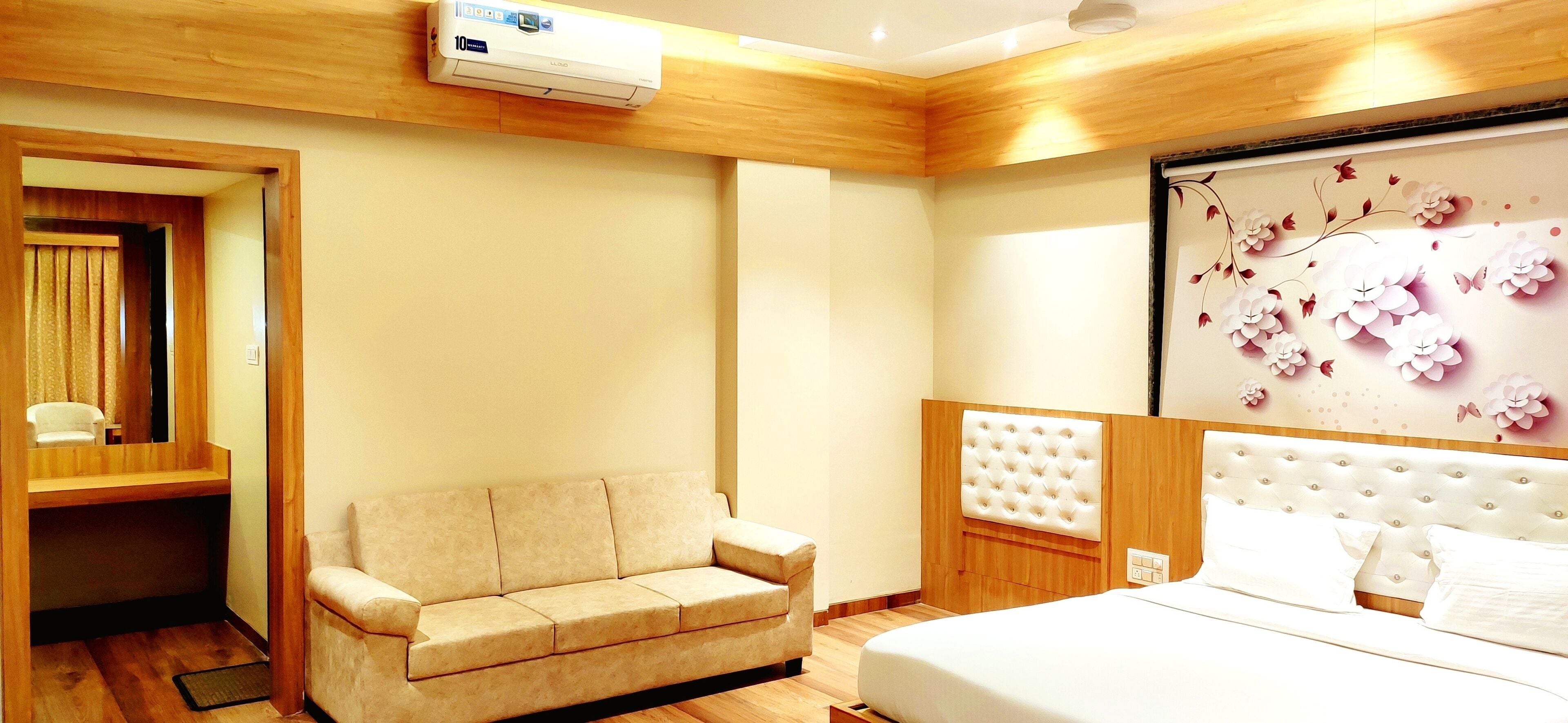 A hotel room with a bed, a sofa, a wooden ceiling, and a wall-mounted air conditioner.