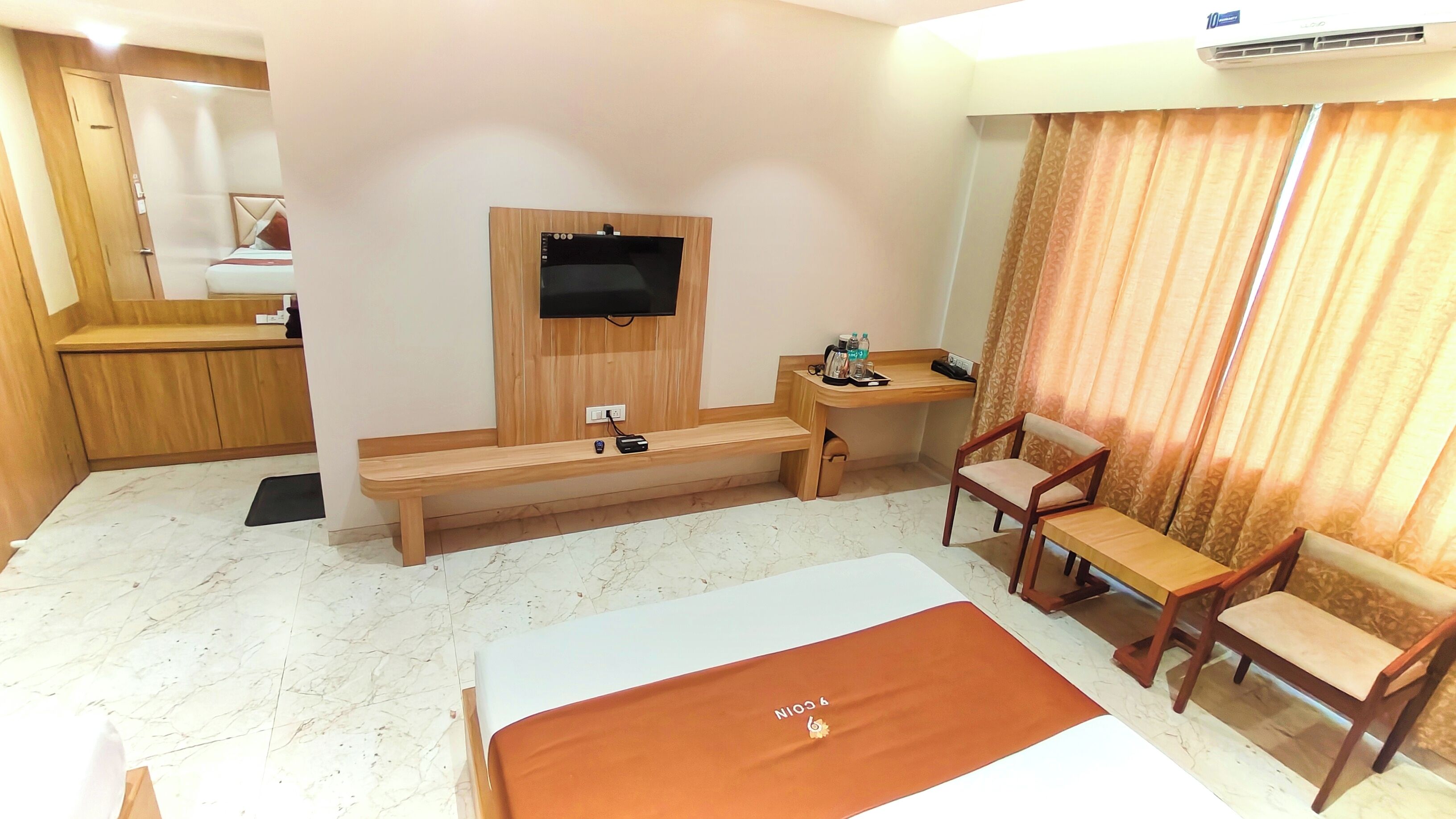 A hotel room with a bed, a desk, a chair, a TV, and a small table with a bottle of water and a cup.
