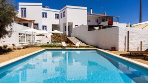 A swimming pool with lounge chairs, a stone staircase, and a white building with blue trim. - A Casa da Cerca (Almodôvar)