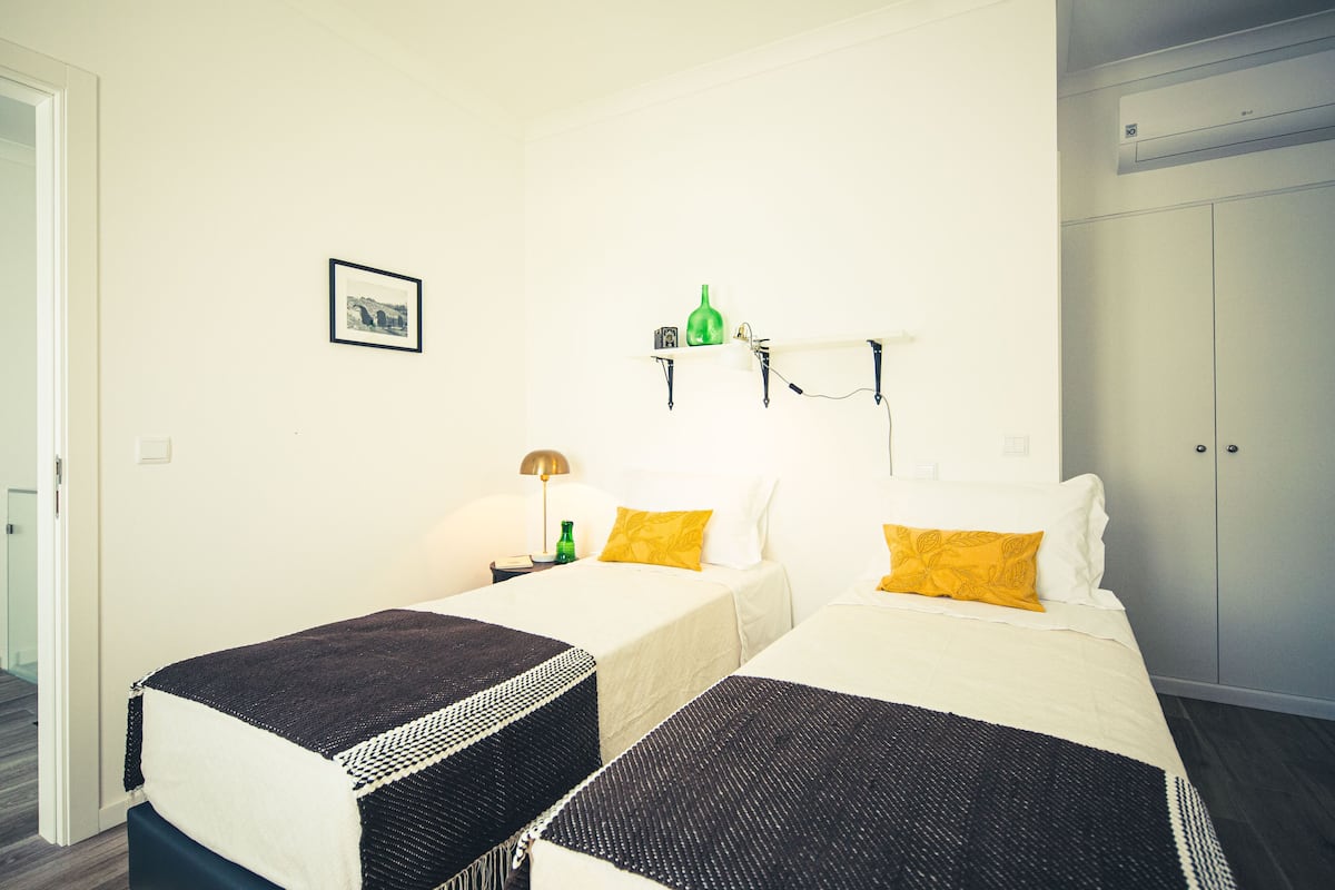Ett hotellrum med två sängar, en liten hylla med en grön flaska och en tavla, en lampa och en garderob.