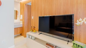 Een moderne woonkamer met een flatscreen televisie bevestigd aan een houten wand, een witte console tafel eronder en een klein decoratief schap met beeldjes.