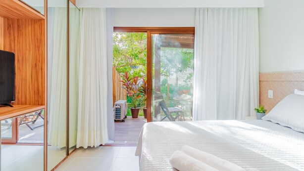 Hotelkamer met een groot bed, een televisie op een houten standaard, een balkon met een tafel en stoelen, en een potplant.