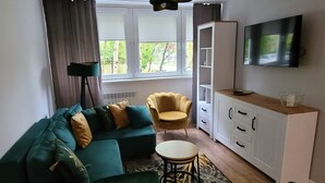 Una sala de estar moderna con un sofá seccional verde, un sillón amarillo, una mesa de comedor de madera y un televisor montado en la pared.