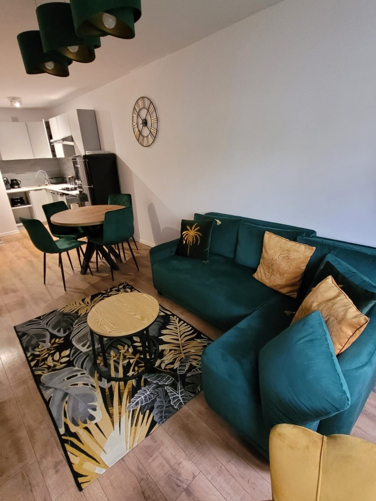 Ein modernes Wohnzimmer mit einem türkisfarbenen Sofa, einem runden Couchtisch und einem Essbereich mit einem Holztisch und Stühlen.