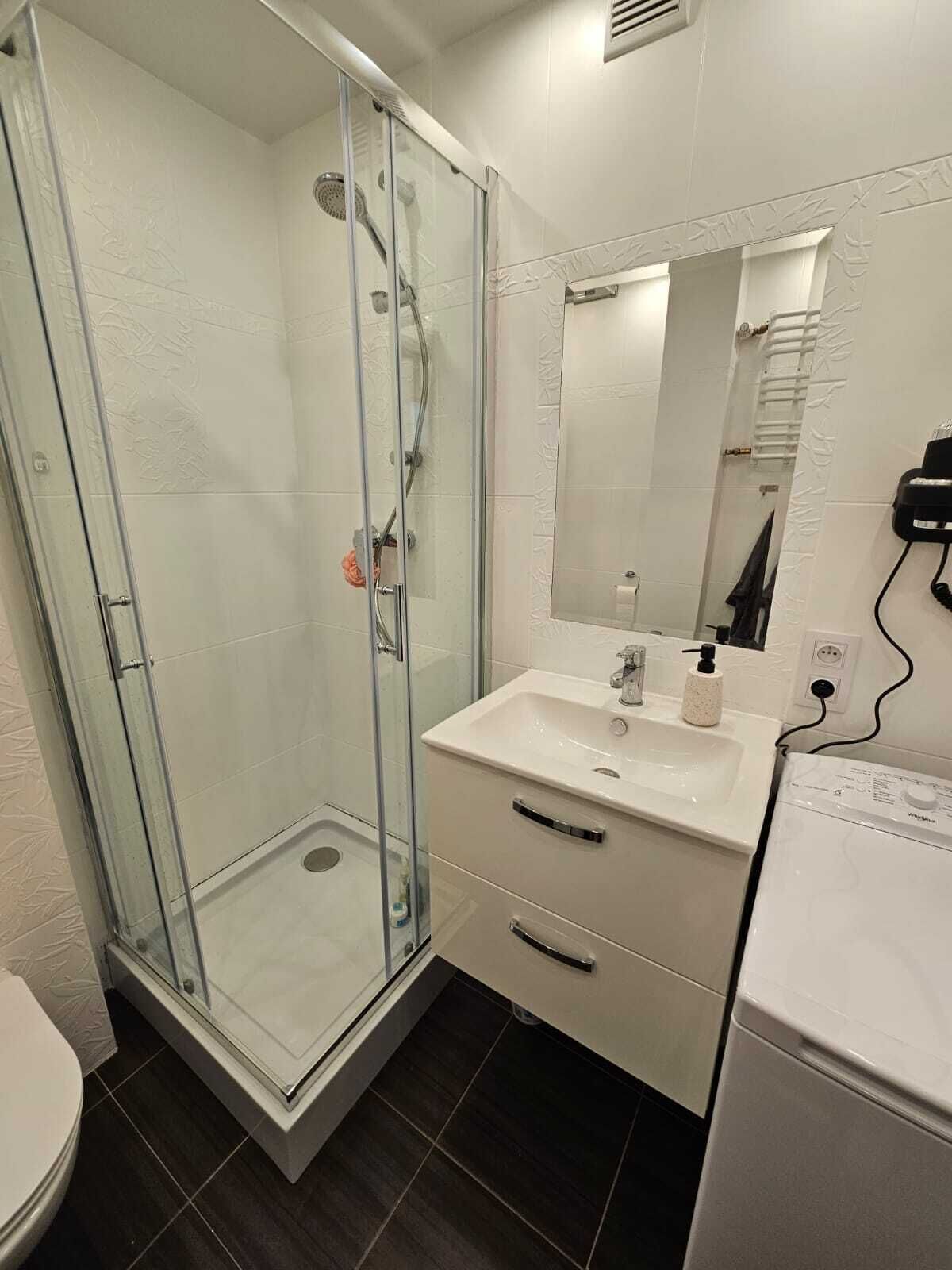 Une salle de bain avec une douche à parois de verre, un lavabo blanc avec un miroir au-dessus et des toilettes blanches.