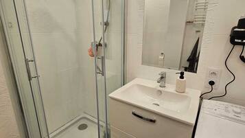 Une salle de bain avec une douche à parois de verre, un lavabo blanc avec un miroir au-dessus et des toilettes blanches.