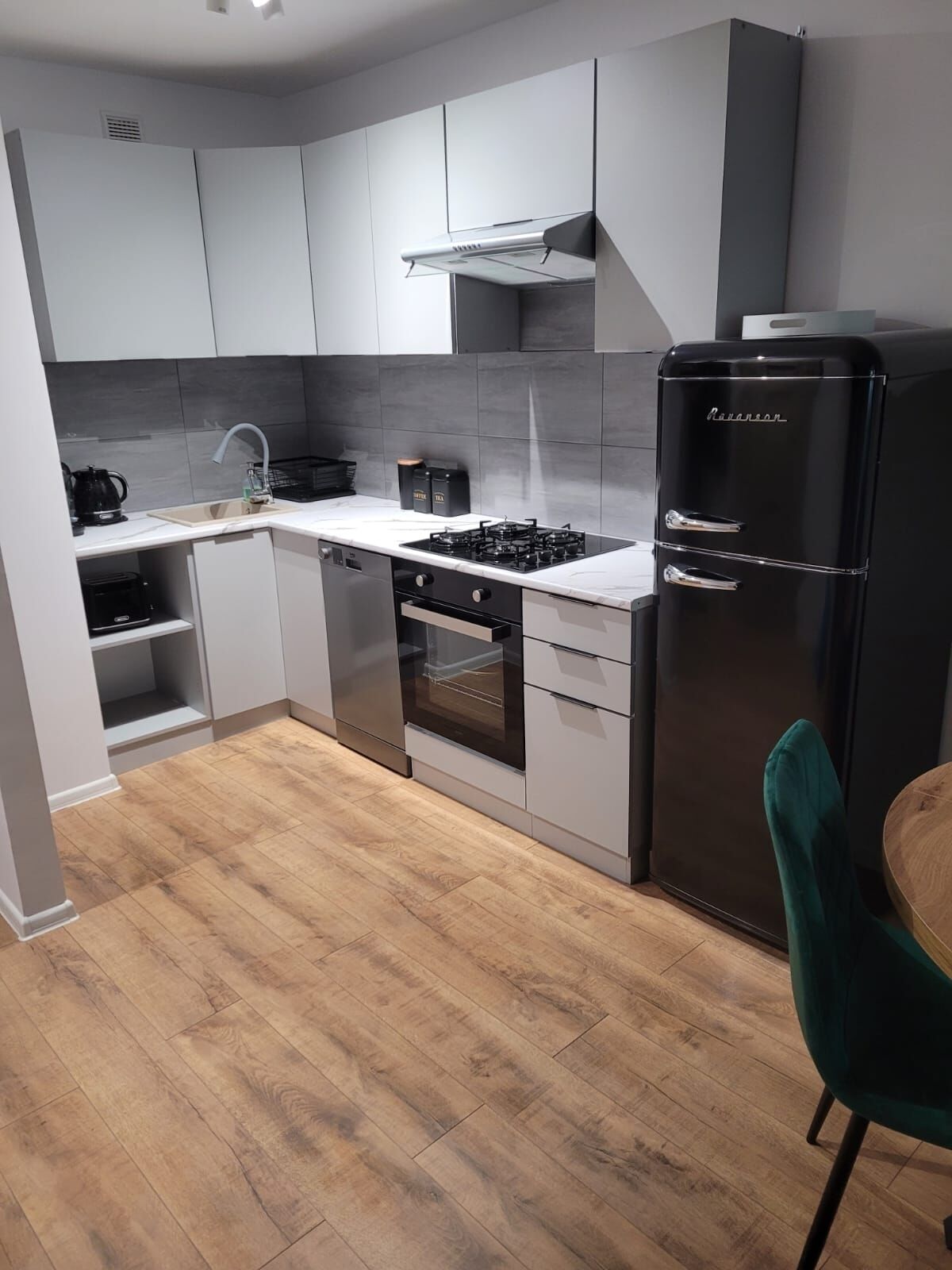 A modern kitchen with grey cabinets, a black refrigerator, a stove, and a sink.