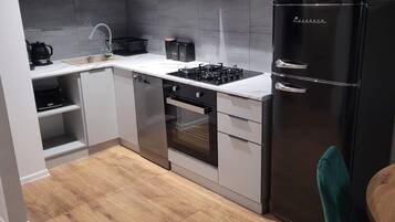 A modern kitchen with grey cabinets, a black refrigerator, a stove, and a sink.