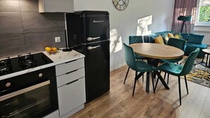 Una cocina moderna con un refrigerador negro, una estufa y un comedor con una mesa redonda y sillas color esmeralda.