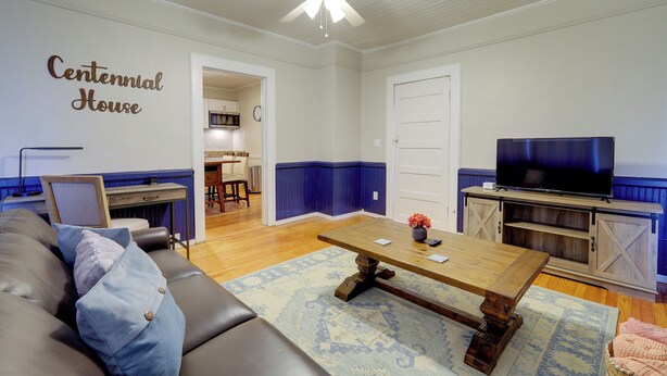 Een woonkamer met een houten salontafel, een leren bank, een televisie op een houten dressoir, en een muur met de tekst 