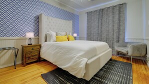 Een slaapkamer met een groot bed, een nachtkastje, een stoel, een plafondventilator en behang met een patroon.