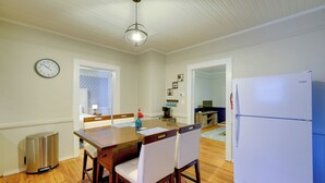 Een eethoek met een houten tafel, twee stoelen, een witte koelkast en een prullenbak.