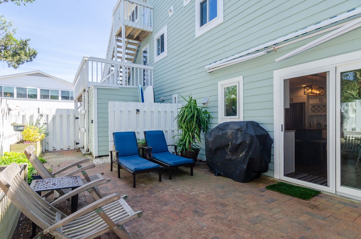 A patio area with two blue lounge chairs, a wooden table, and a barbecue grill.