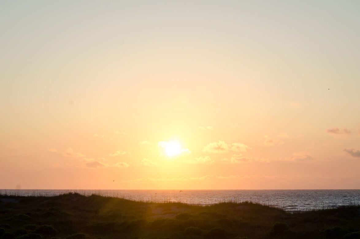 Een zonsondergang boven een strand met een heldere lucht en een kalme zee.