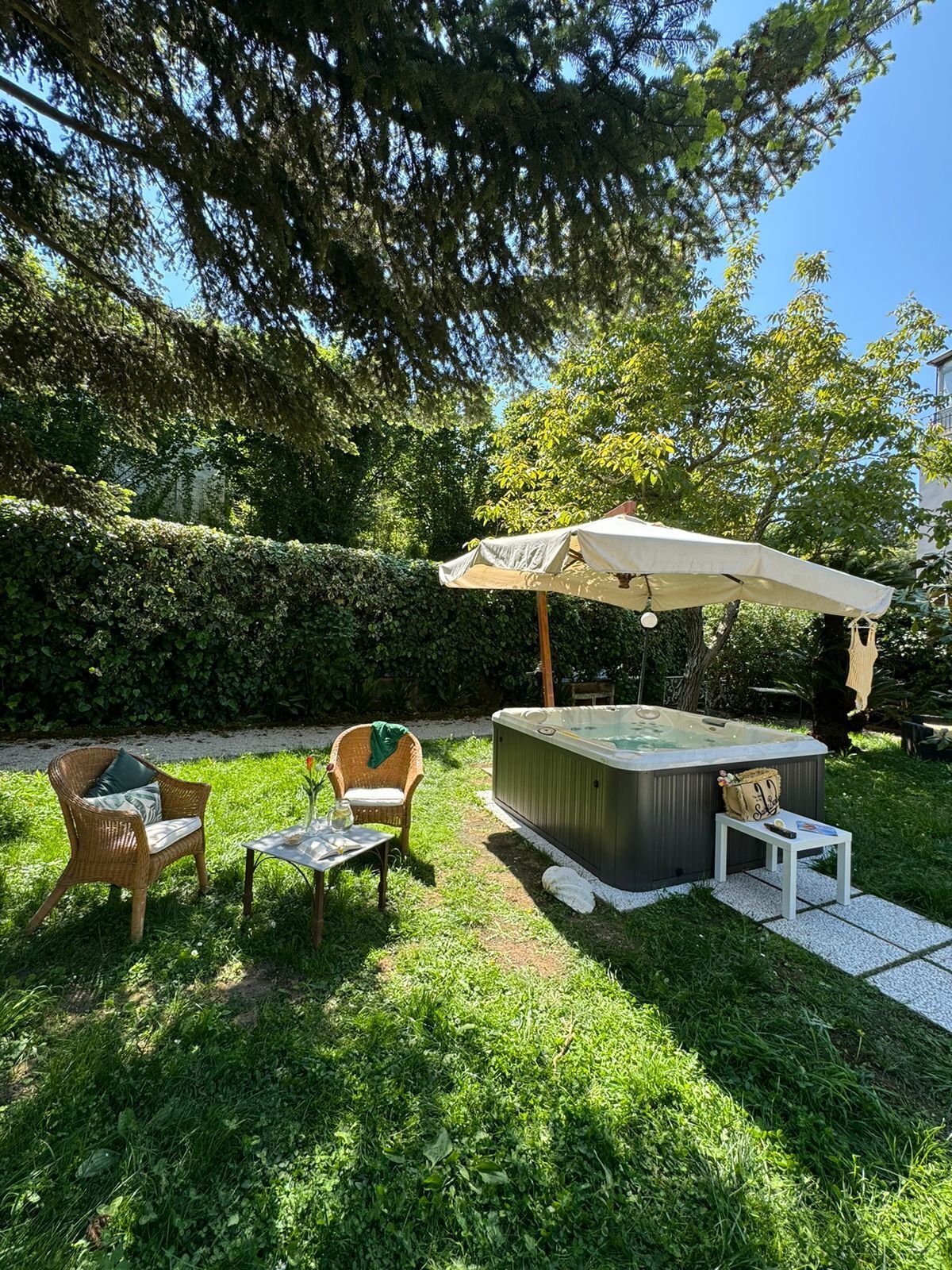 Un bain à remous avec un parasol, deux fauteuils en osier, une petite table et une haie, le tout installé dans un jardin.