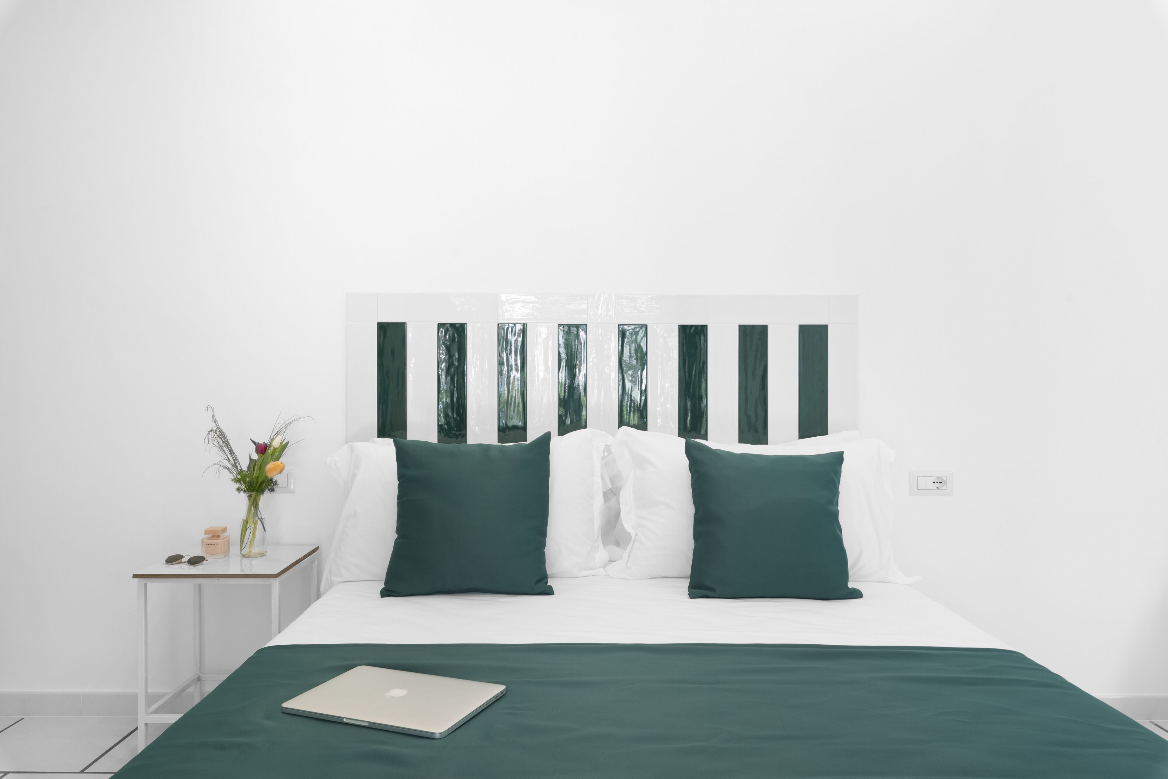 Un dormitorio ordenado con una cama, una mesita de noche con una computadora portátil y una planta pequeña.