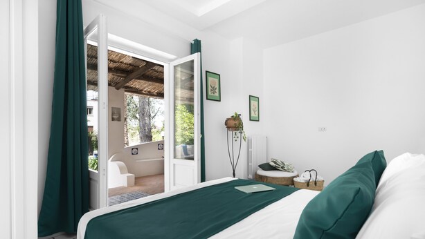 Ein Schlafzimmer mit Bett, Nachttisch, einem Fenster mit Vorhängen und Blick nach draußen.