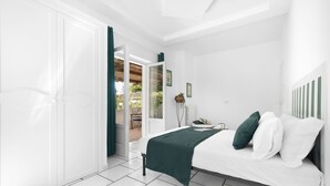 Ein Schlafzimmer mit einem Bett, einem Nachttisch, einem Sessel und Blick auf eine Terrasse.