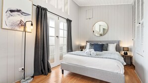 A bedroom with a bed, bedside lamps, a round mirror, and a window with curtains. - Loft Ninety Three | Stylish & Central (Orange)