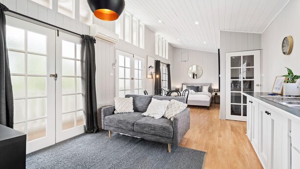 A modern interior with a grey sofa, a kitchen area, and a large window. - Loft Ninety Three | Stylish & Central (Orange)