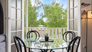 An open patio with a glass table and chairs, a potted plant, and a view of trees and sky. - Loft Ninety Three | Stylish & Central (Orange)