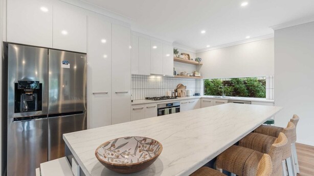 A modern kitchen with white cabinetry, a stainless steel refrigerator, a built-in stove, and a large island with a bowl. - Shepherds Delight-Disabled/Access Friendly (Goolwa South)