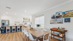 A modern kitchen with white cabinets, a wooden dining table, and a large window. - Shepherds Delight-Disabled/Access Friendly (Goolwa South)
