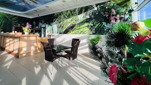 Un interior moderno con una recepción, zona de estar y un gran mural de paisaje tropical.