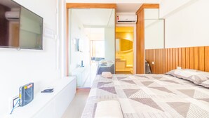Ein modernes Hotelzimmer mit einem großen Bett, einem an der Wand befestigten Fernseher und einem durch eine geöffnete Tür einsehbaren Badezimmer.