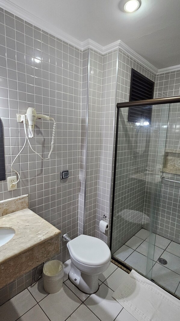 Un baño con inodoro, lavamanos, cabina de ducha de vidrio y un teléfono en la pared.
