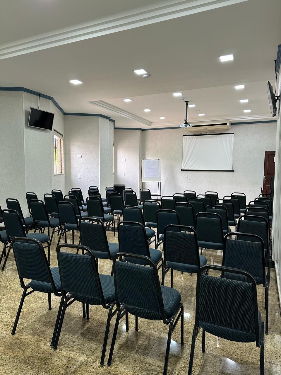 A conference room with rows of chairs, a projector screen, and a whiteboard.