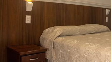 A bedroom with a wooden nightstand, a bed with a patterned bedspread, and a wall-mounted light fixture.