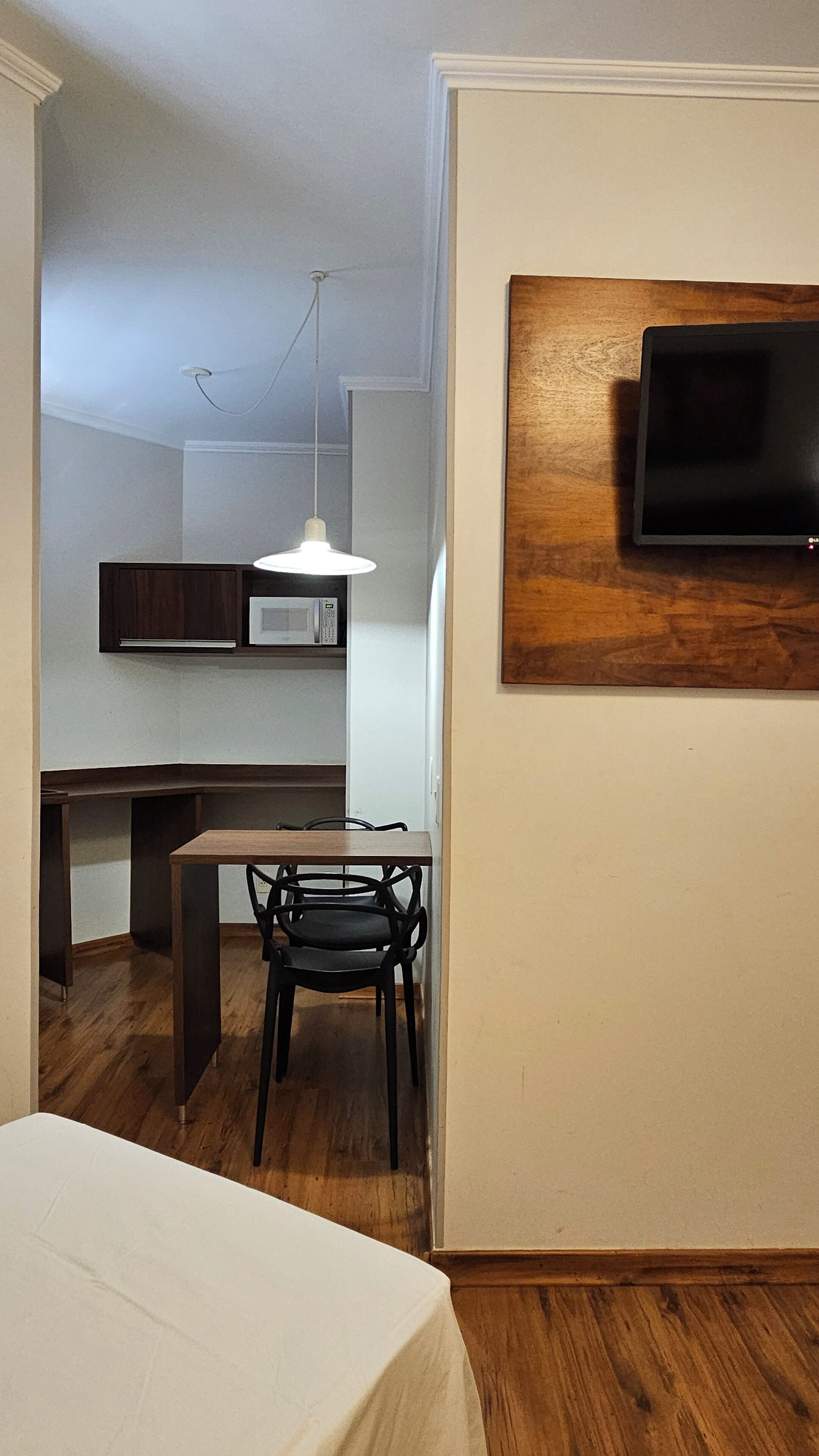 A compact living space with a kitchenette, a dining area with a table and chairs, and a TV mounted on a wall.