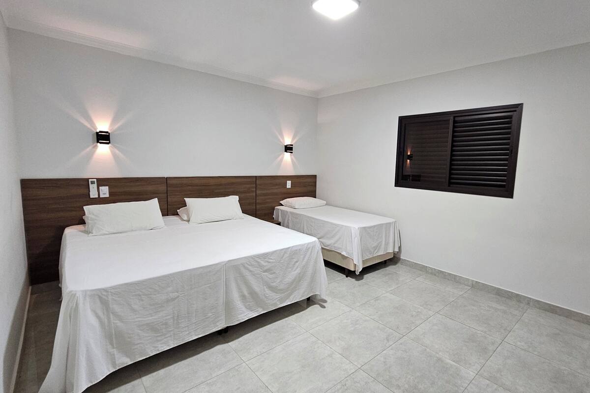 Een hotelkamer met twee bedden, een houten hoofdbord, witte beddengoed en twee wandlampen.