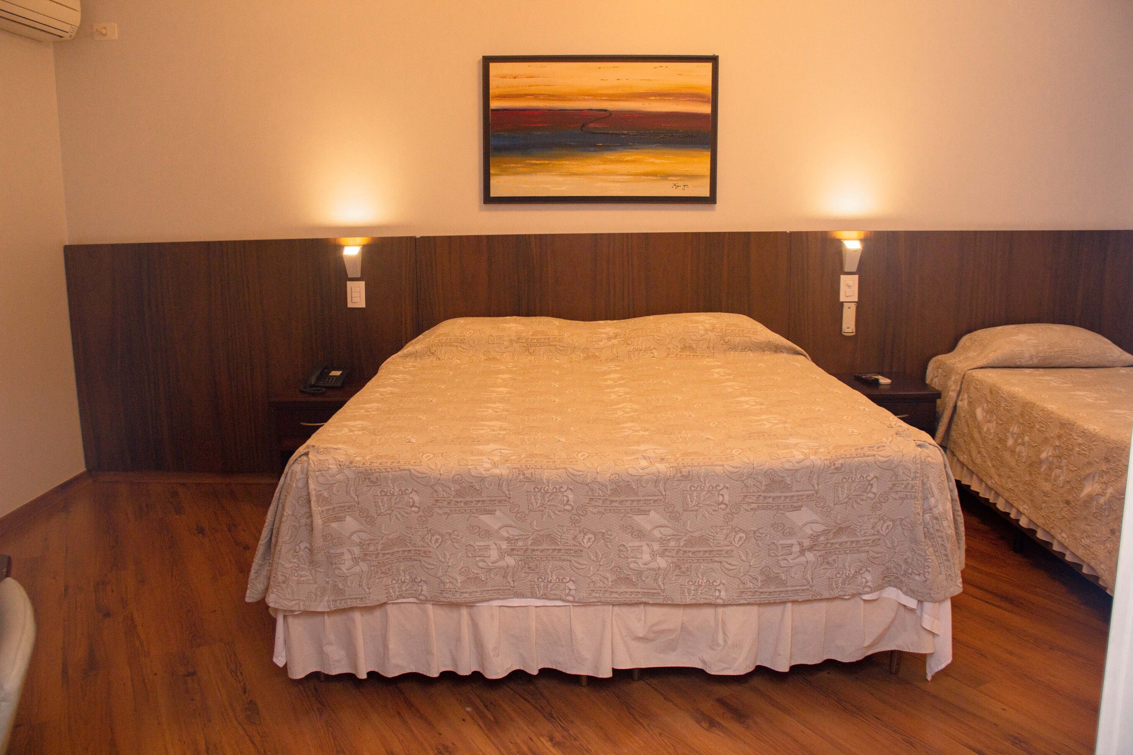 Quarto de hotel com uma cama grande, duas mesas de cabeceira e um quadro na parede.