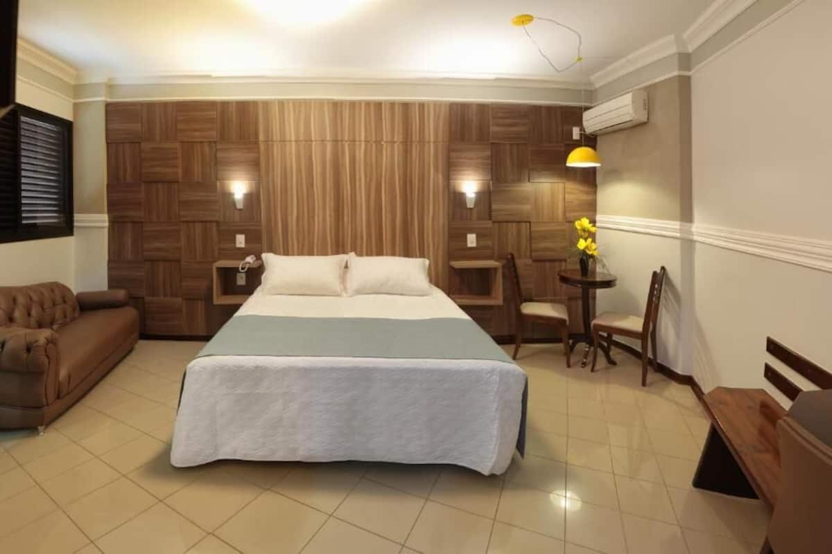 Een hotelkamer met een groot bed, een bank, een tafeltje met een bloevas en een bureau.