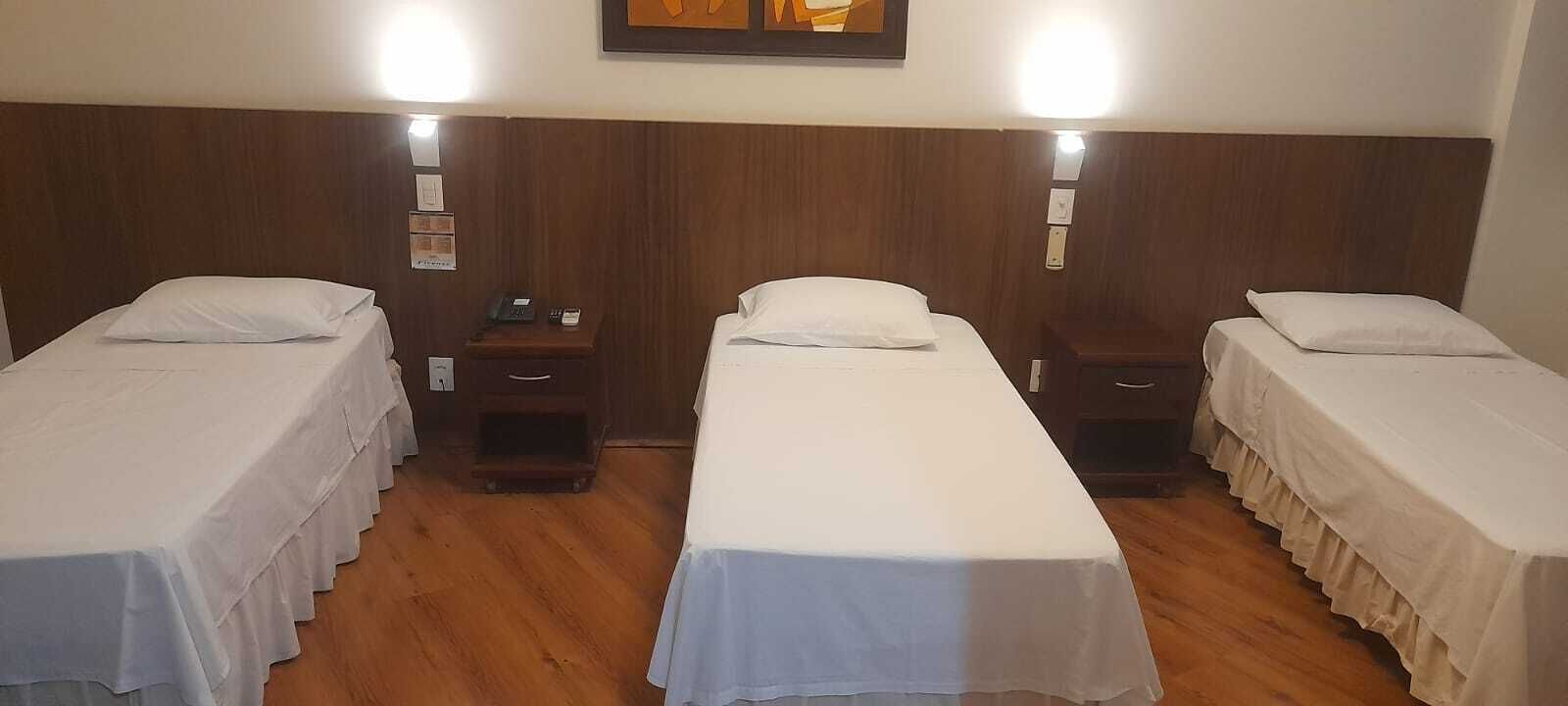 Ein Hotelzimmer mit drei Einzelbetten, Holz-Kopfteilen, Nachttischen und Wandlampen.