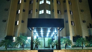 A multi-story hotel with a central entrance, palm trees, and a stone wall.