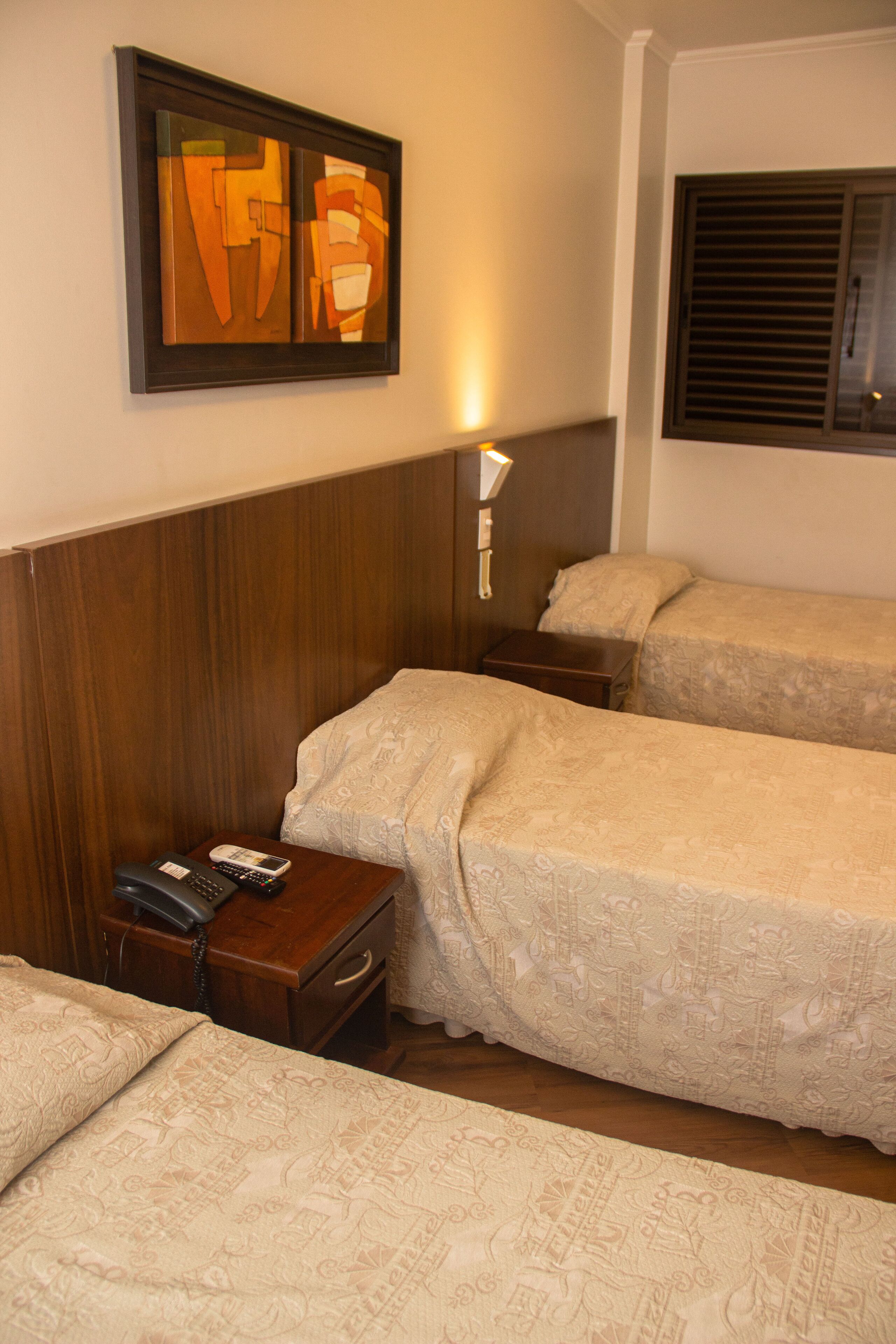 Habitación de hotel con dos camas, cabecero de madera, mesita de noche con teléfono y un cuadro en la pared.