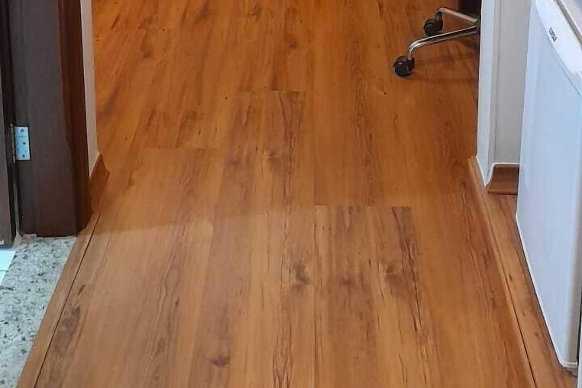 Een hotelkamer met een houten vloer, een bed met wit beddengoed, een bureau met een stoel en een airconditioning.