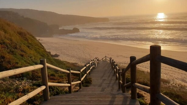 A wooden staircase leading to a beach with a wooden railing, overlooking the ocean and a sunset. - Sunset Milfontes (Odemira)