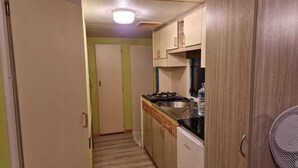 A narrow kitchen with wooden cabinets, a gas stove, and a sink. - Sunset Milfontes (Odemira)