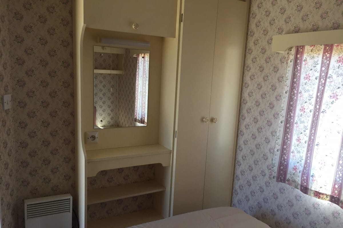 A bedroom with a bed, a wardrobe, a mirror, and a window with curtains.