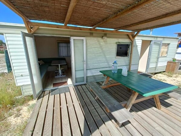 Une maison mobile dotée d’un espace extérieur couvert, d’une table de pique-nique et d’une porte coulissante donnant sur une petite pièce avec un lit et une fenêtre.