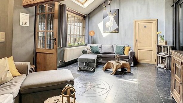 A cozy living room with a high ceiling, exposed wooden beams, a large window, a fireplace, and a comfortable seating area. - Gite Chalet in the Ardenne, Houffalize. Authentic but Renewed House for 9 People (Houffalize)